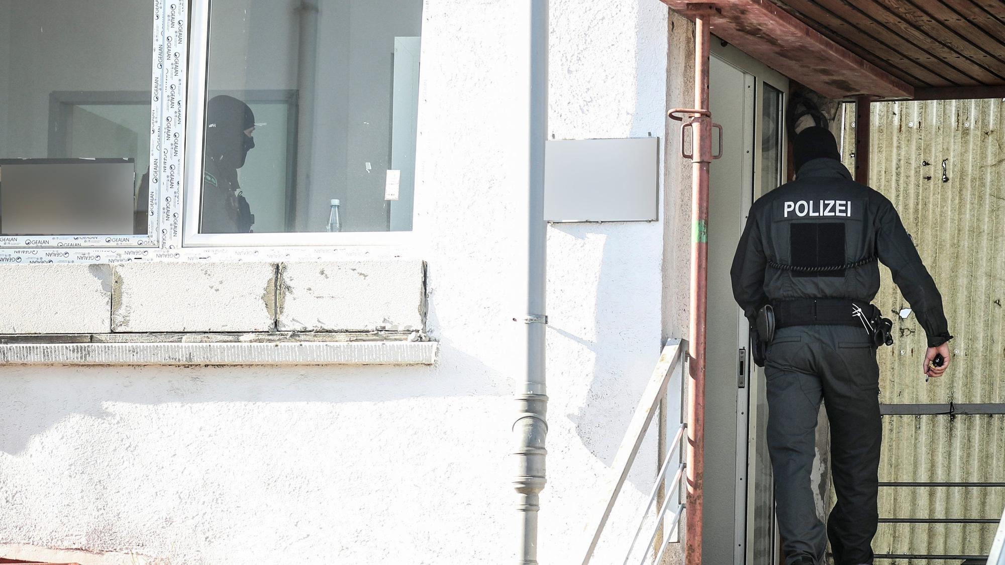 Einsatzkräfte der Polizei durchsuchen bei einer bundesweiten Razzia eine Moschee. Ein Beamter ist von hinten zu sehen in schwarzer Kleidung, er betritt ein weiß verputztes Gebäude.