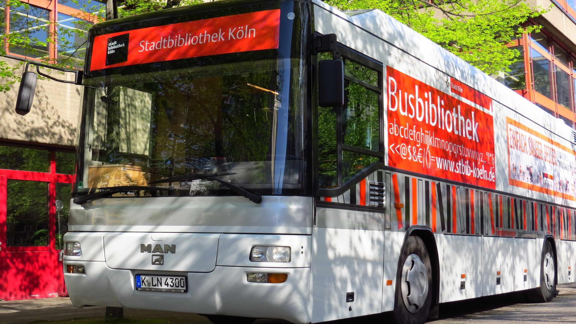 Ein Bücherbus mit der Aufschrift „Busbibliothek“ parkt vor einem großen Gebäude.