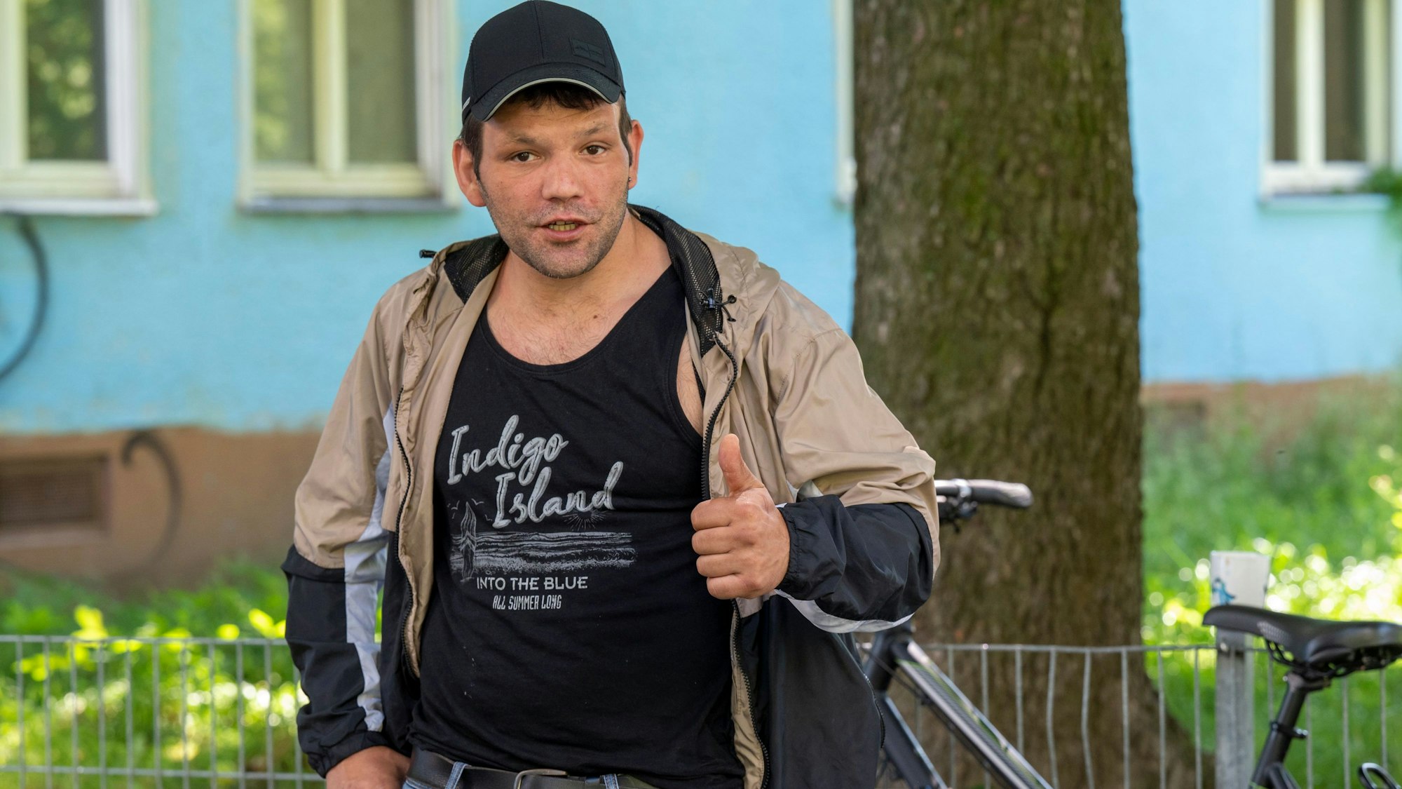 Mann mit einem schwarzen Tanktop, einer beigen Jacke und einer schwarzen Mütze