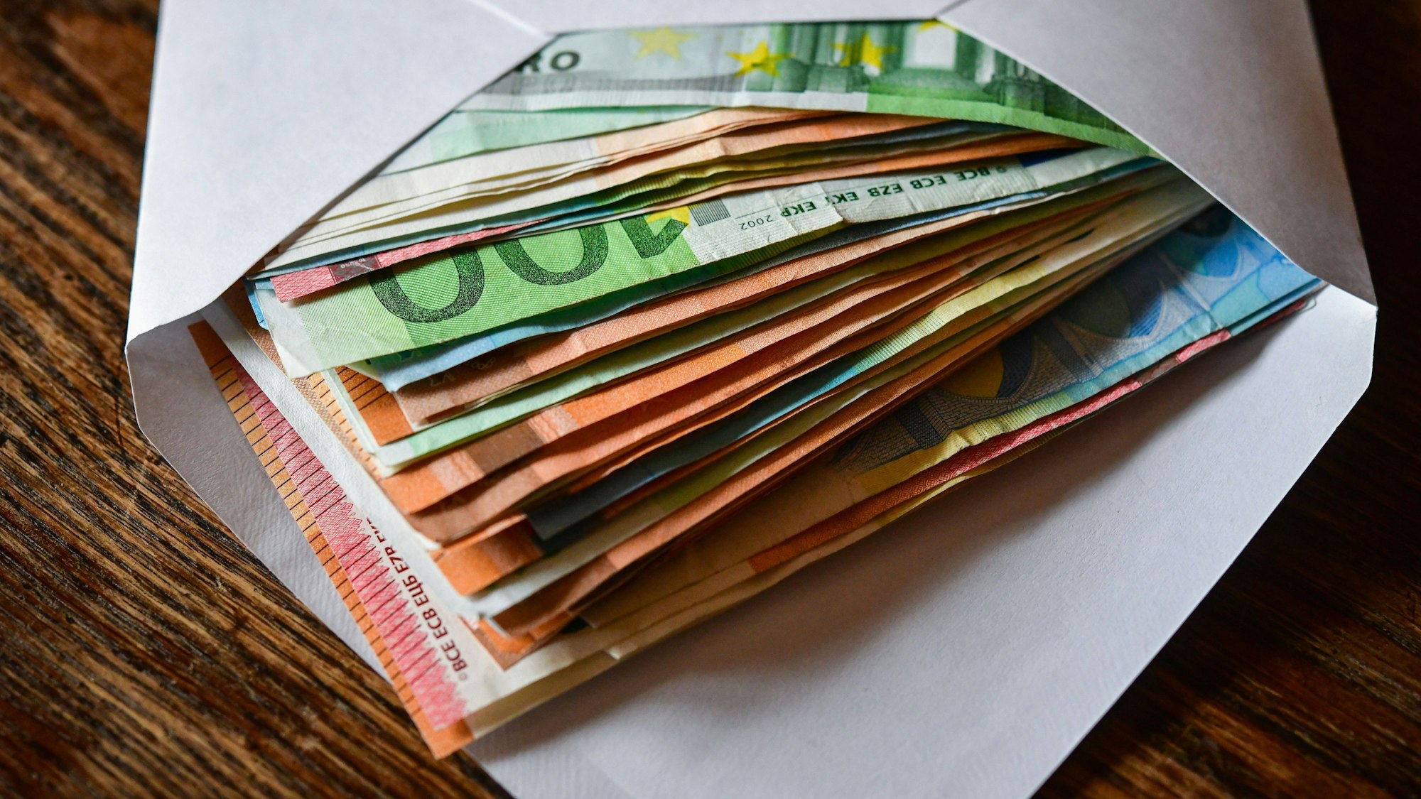 Viele Eurobanknoten liegen in einem Briefumschlag auf einem Tisch.