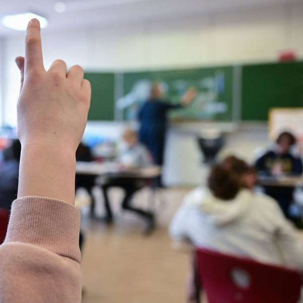 Ein Kind hebt in einer vollbesetzten Klasse den Finger.