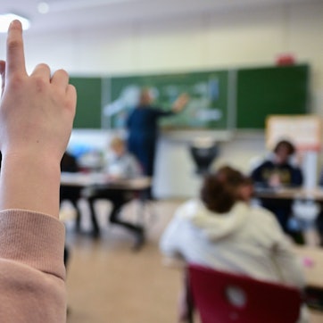 Ein Kind hebt in einer vollbesetzten Klasse den Finger.