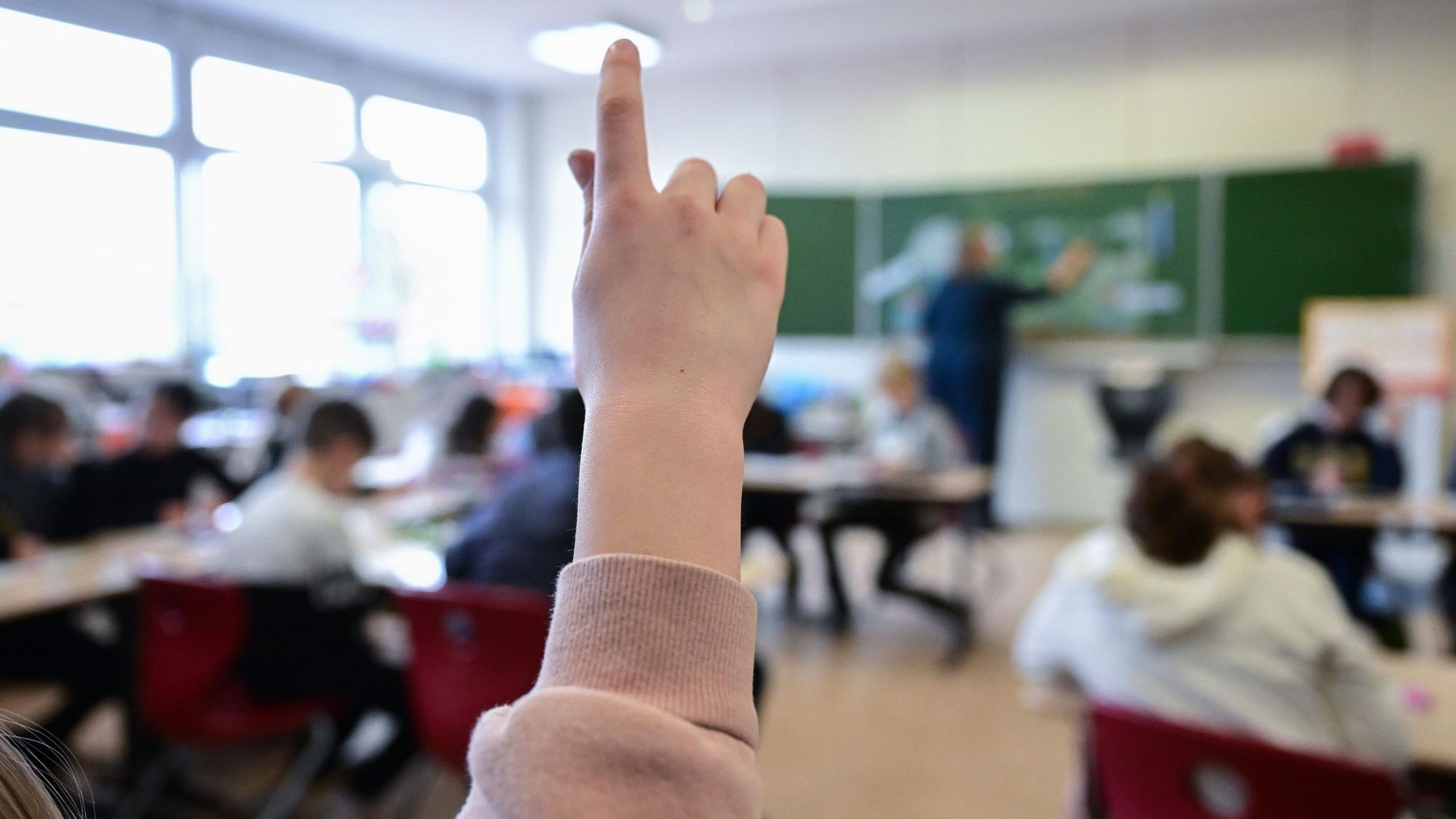 Ein Kind hebt in einer vollbesetzten Klasse den Finger.