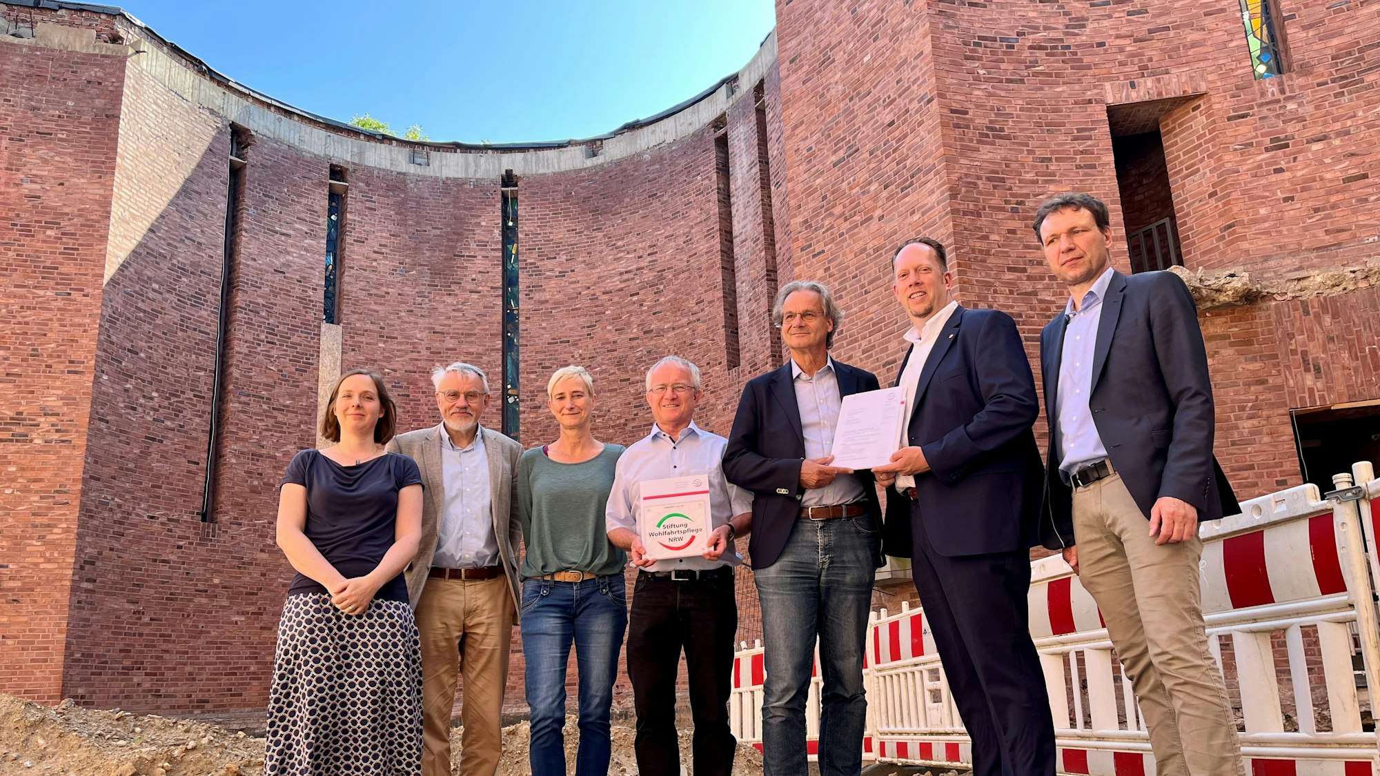 Sieben Menschen mit Plakette und Förderbescheid im Inneren der Kirchmauern