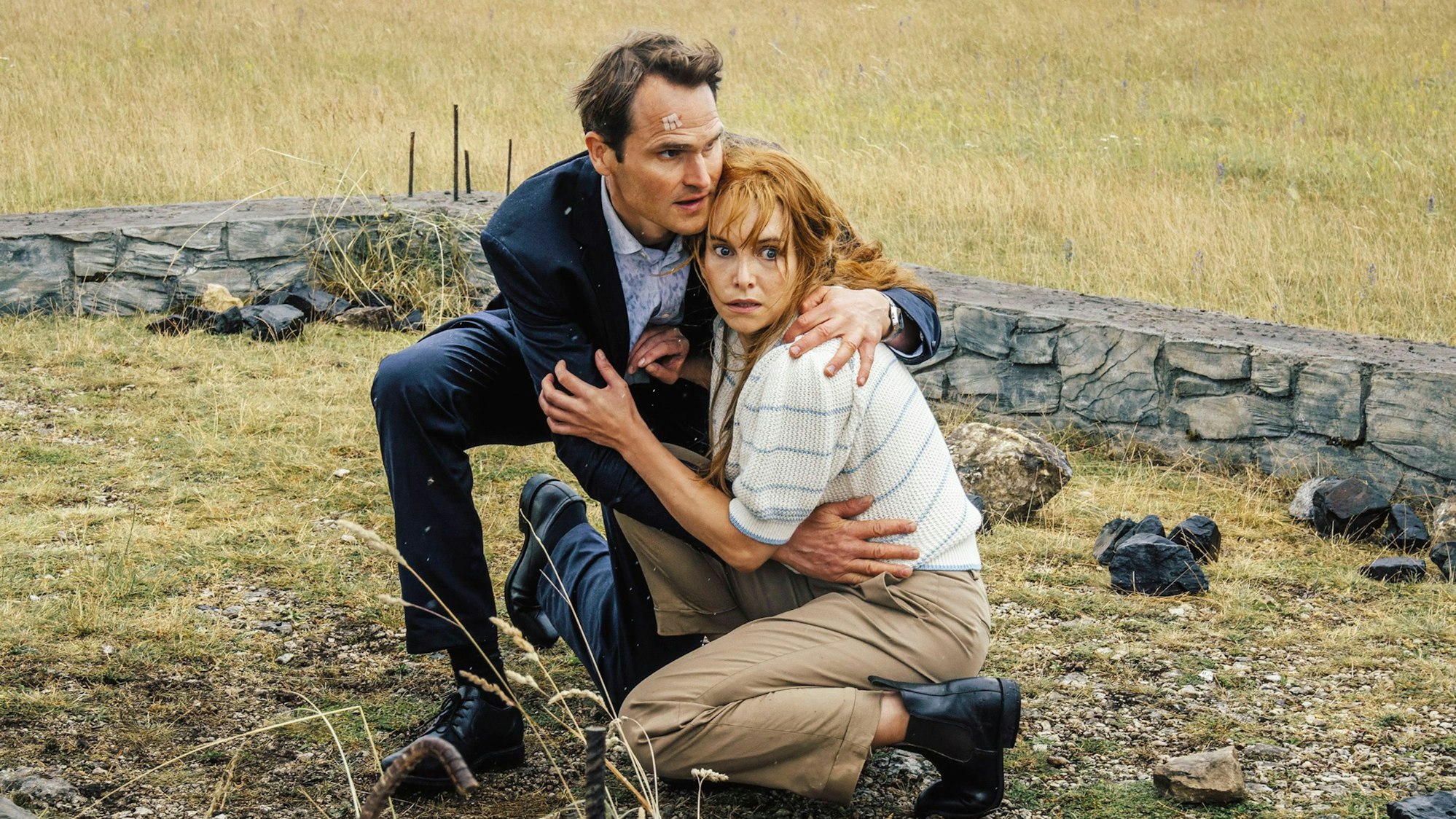 Felix Voss (Fabian Hinrichs) und Eva Hentschel (Sina Martens) gehen in Deckung. Hinter ihnen sieht man die steinernen Überbleinsel einer Hütte.