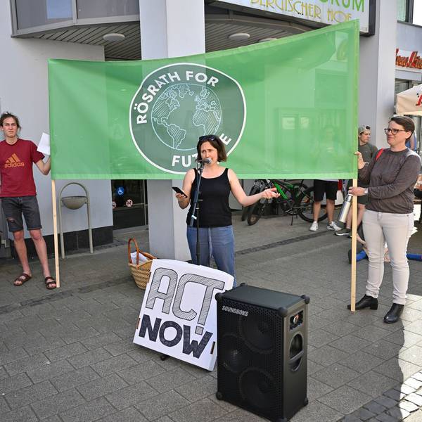 Eine Aktivistin hält eine Rede. Hinter ihr halten zwei Menschen ein Banner mit der Aufschrift „Rösrath for Future“.