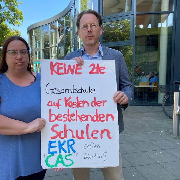 Es sind zwei Menschen zu sehen, die ein Schild hochhalten, auf dem steht: „Keine 2te Gesamtschule auf Kosten der bestehenden Schulen“.