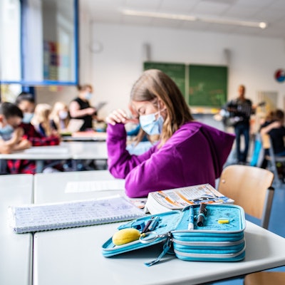 Eine Schülerin sitzt mit ihrer Maske neben ihrem Etui, das auf ihrem Tisch in der Klasse liegt.