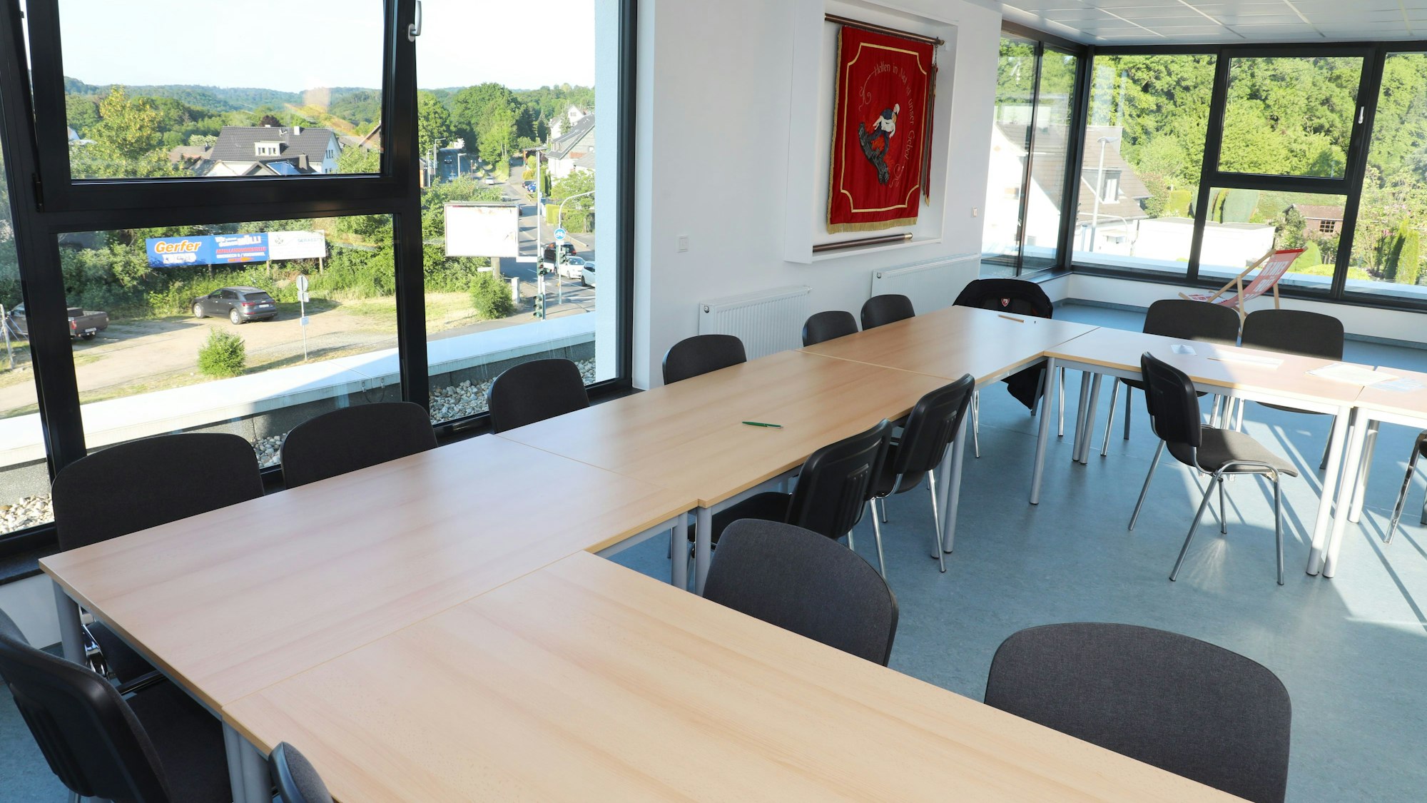 In einem Raum mit großen Fenstern, die den Blick auf einen Ort freigeben, stehen Tische. An der Wand hängt eine Feuerwehrfahne.