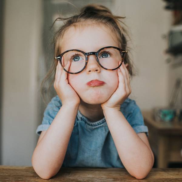 Ein kleines Mädchen mit einer großen, runden Brille hat sein Gesicht auf seine Hände gestützt und schaut sehr gelangweilt aus.