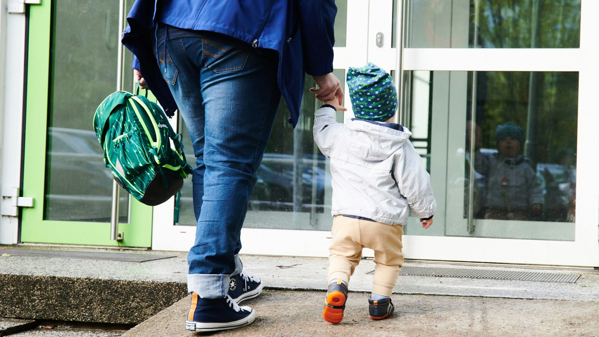 Ein Kind und seine Mutter gehen zum Eingang einer Kita.