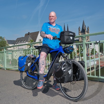 Oliver Trelenberg steht mit seinem Fahrrad auf der Brücke, im Hintergrund das Köln-Panorama.
