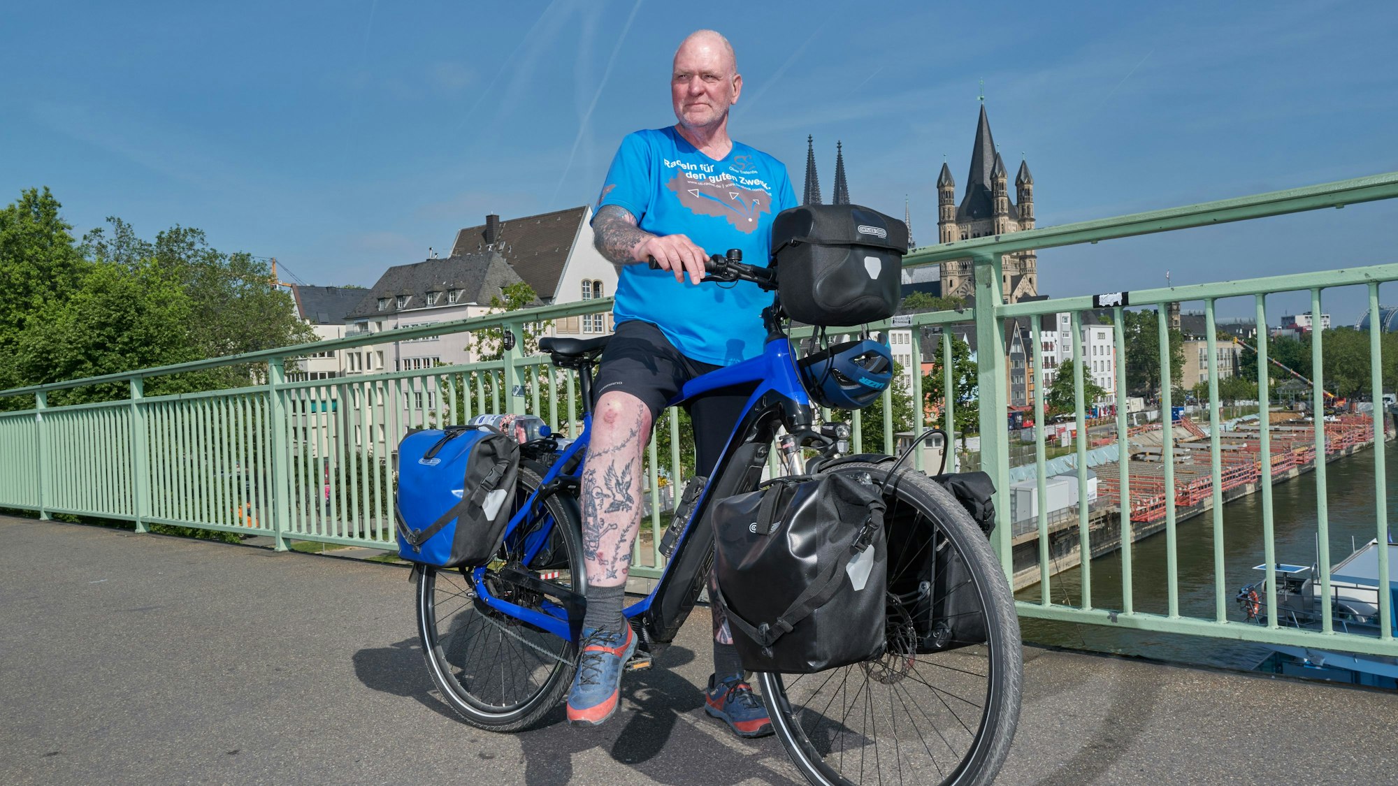Oliver Trelenberg steht mit seinem Fahrrad auf der Brücke, im Hintergrund das Köln-Panorama.