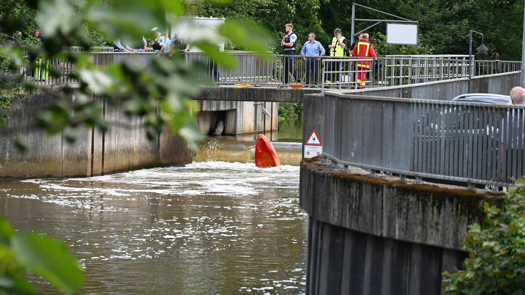 Es ist ein Teil der Erft zu sehen. Auf einer Brücke stehen Rettungskräfte.