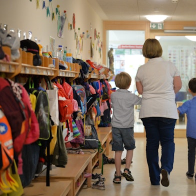 Eine Erzieherin geht mit zwei Kindern über den Flur einer Kita.