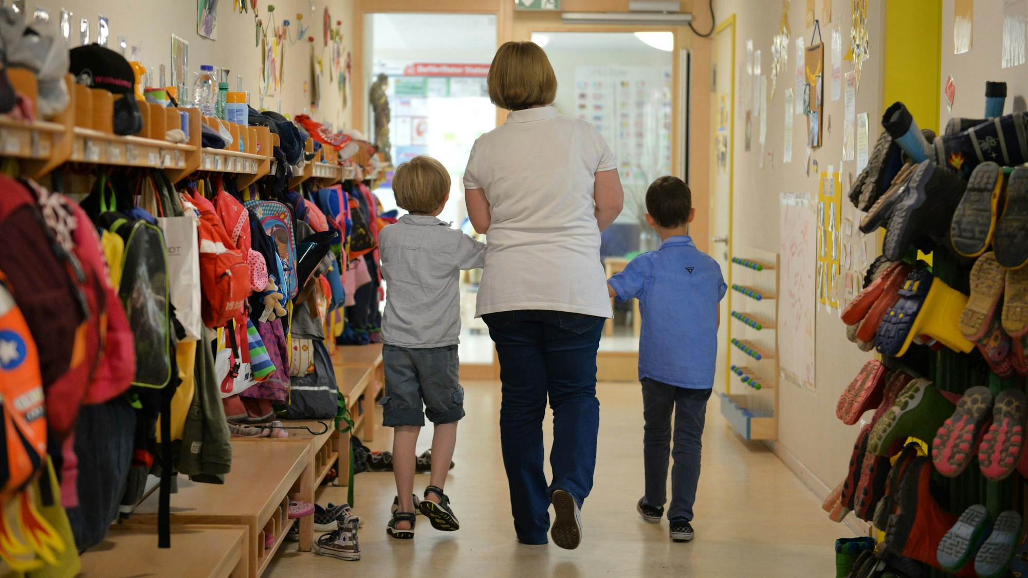 Eine Erzieherin geht mit zwei Kindern über den Flur einer Kita.