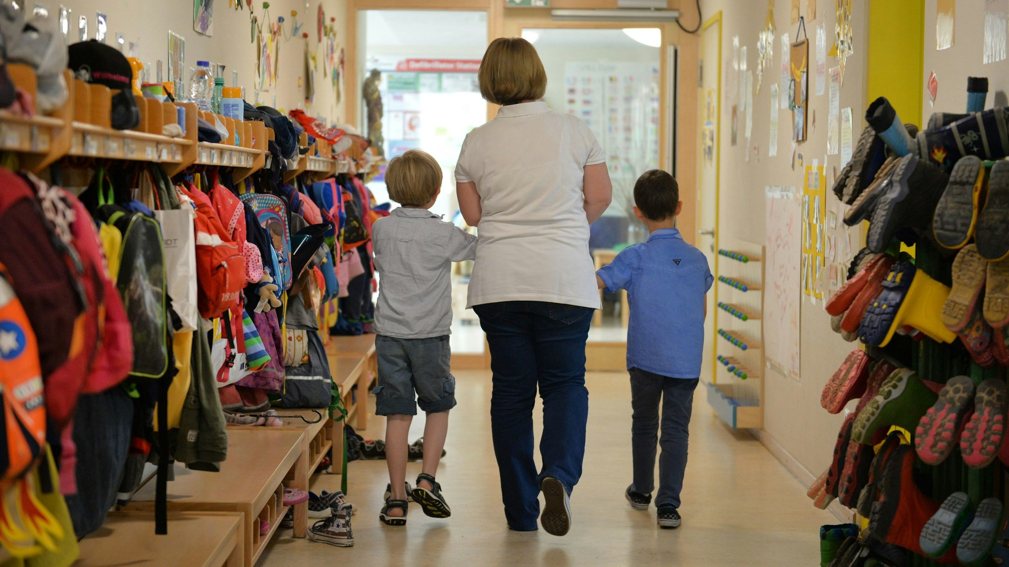 Eine Erzieherin geht mit zwei Kindern über den Flur einer Kita.