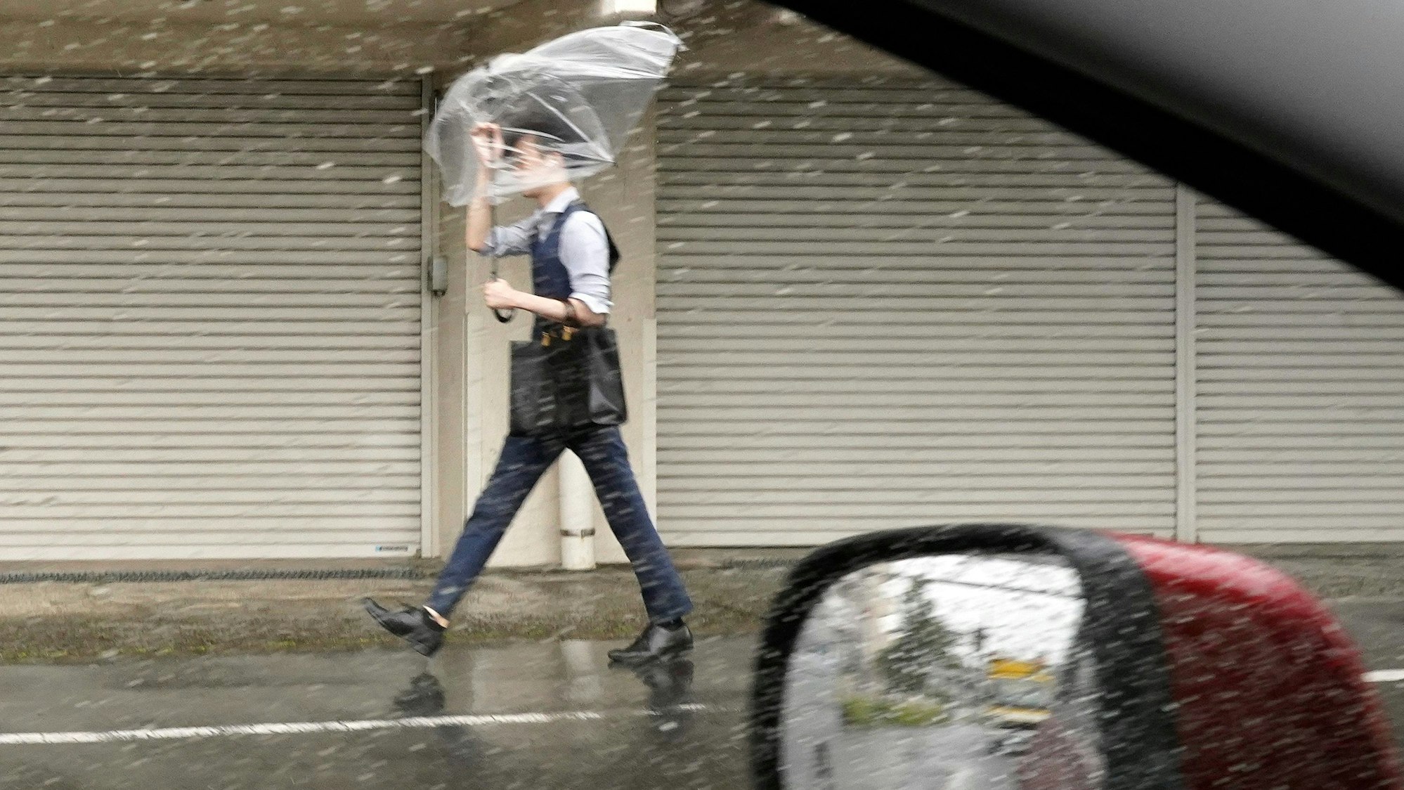 Ein Mann hält einen Regenschirm gegen starken Wind und Regen, während er eine Straße entlang geht.
