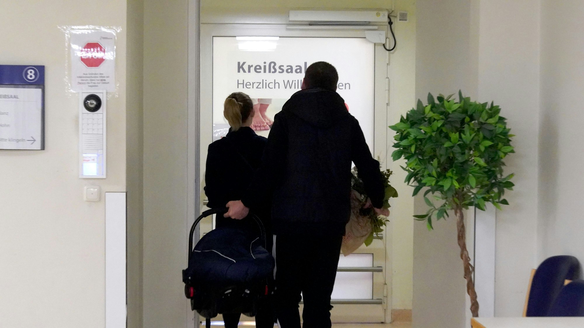 Eine Frau und ein Mann gehen mit einem Baby in den Kreißsaal einer Schwangerenambulanz (Symbolfoto).