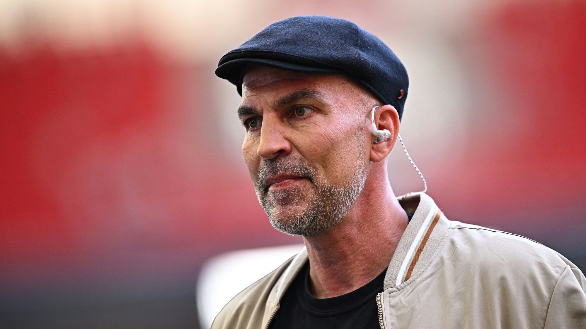 Markus Babbel trägt eine blaue Schiebermütze und eine helle Jacke. Er schaut ernst an der Kamera vorbei.