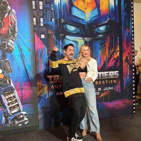 Der Rapper steht mit seiner Frau vor dem Plakat des Films.