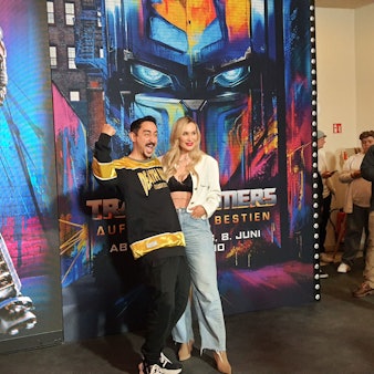 Der Rapper steht mit seiner Frau vor dem Plakat des Films.