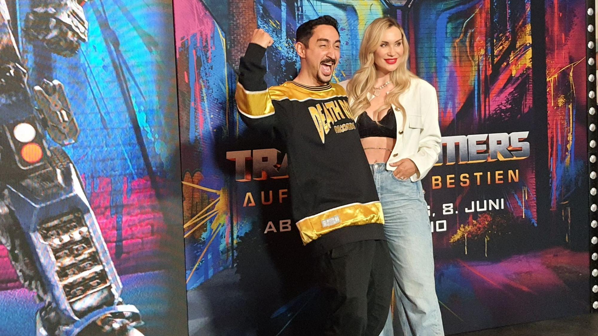 Der Rapper steht mit seiner Frau vor dem Plakat des Films.