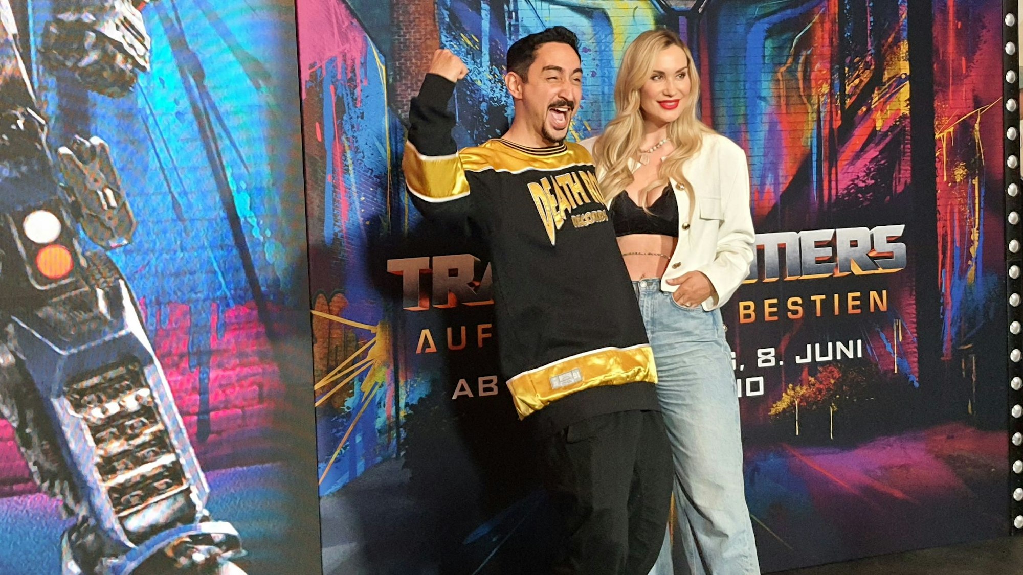 Der Rapper steht mit seiner Frau vor dem Plakat des Films.