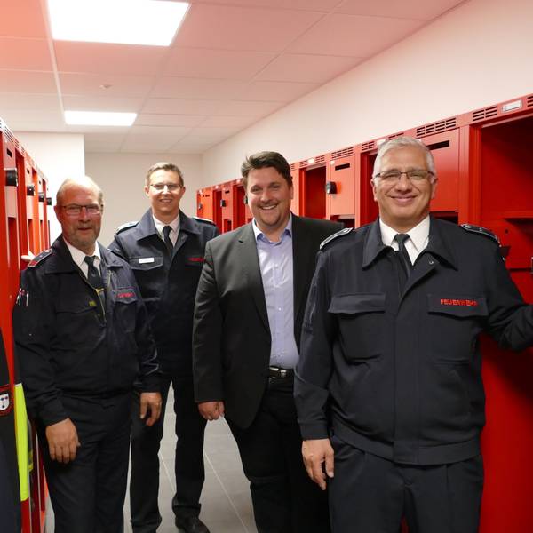 Zu sehen sind Löschgruppenführer Ralf Eich, Leiter der Troisdorfer Feuerwehr, Lars Gödel, Bürgermeister Alexander Biber und Löschgruppenführer Salvatore Rizzello zwischen roten Schränken.