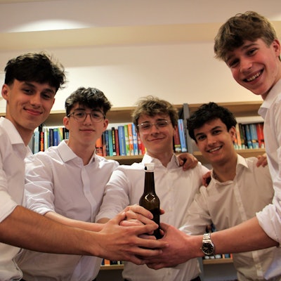 Fünf junge Männer halten gemeinsam eine Bierflasche.