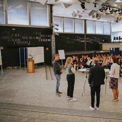 Vier Menschen sprechen vor sitzenden Zuhörern.