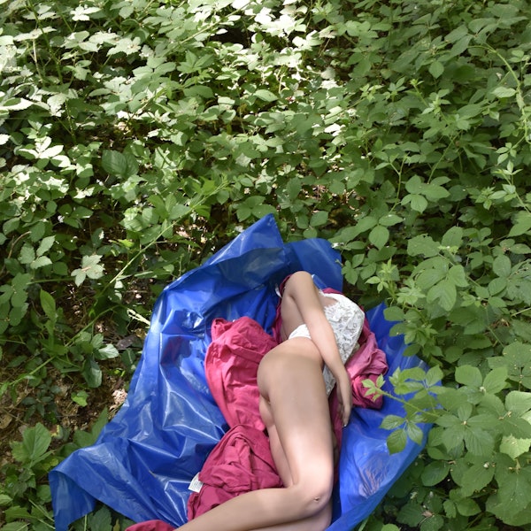 Eine lebensgroße Puppe liegt auf einem Müllsack in einem Gebüsch.