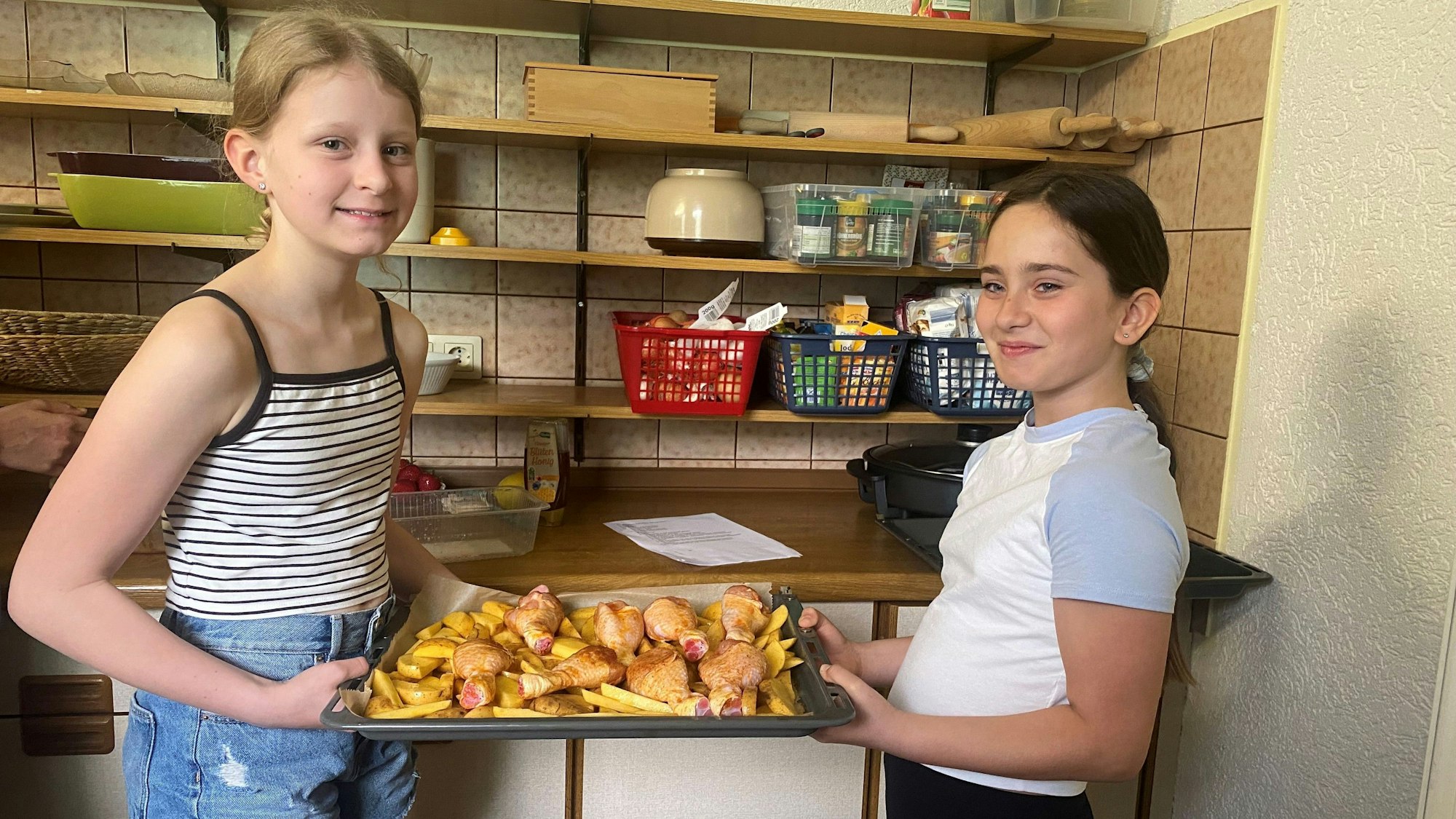 Isabella und Leah mit einem Blech Kartoffeln und Hähnchen