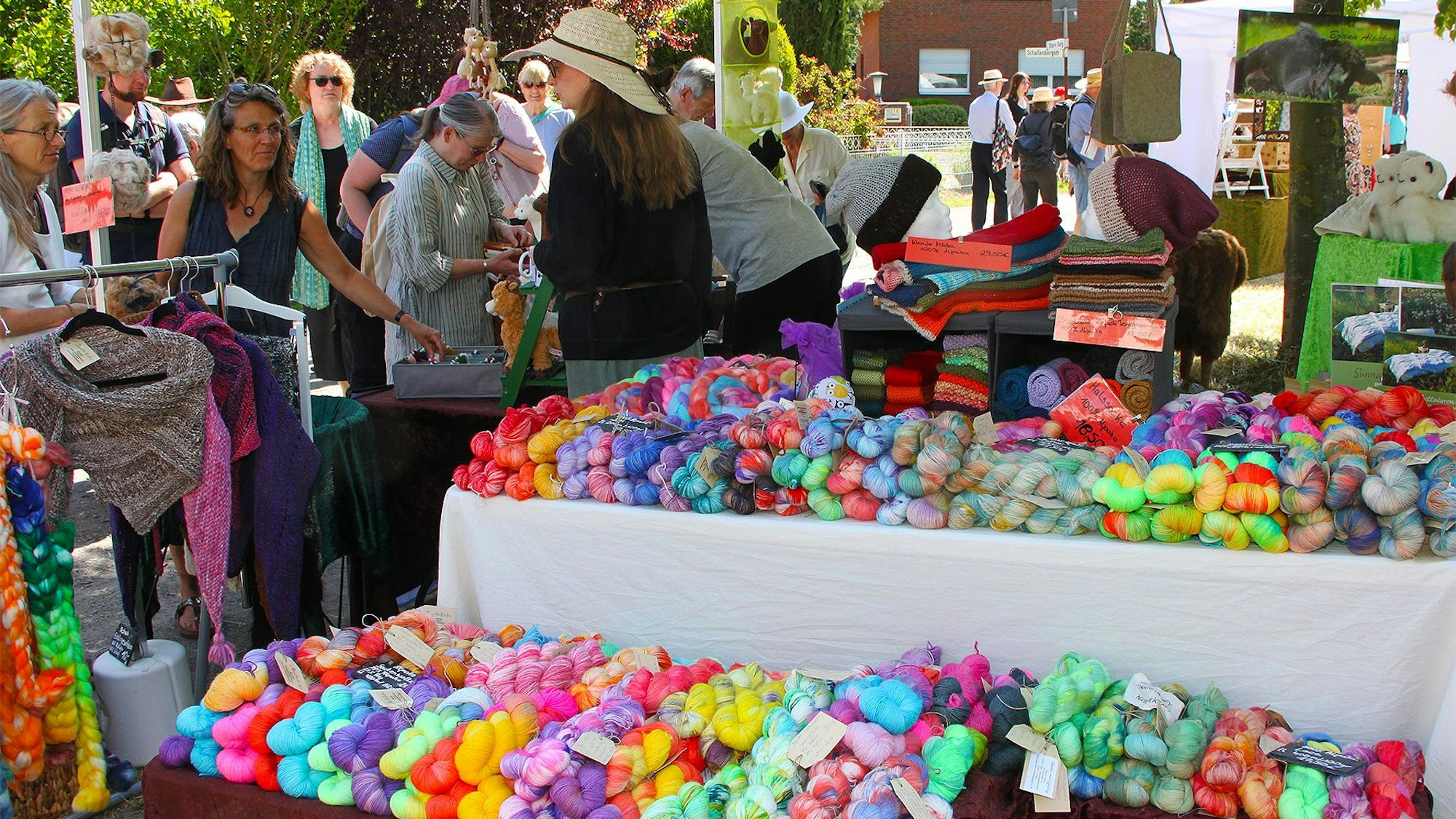 Das Bild zeigt einen Marktstand, auf dem zahlreiche bunte Wollknäuel präsentiert werden.