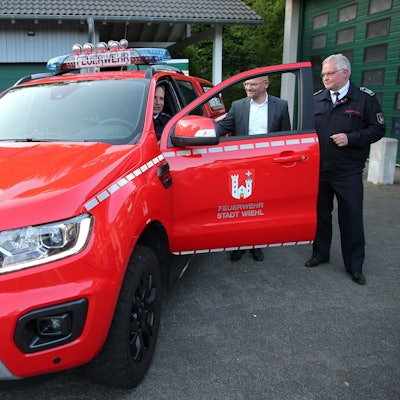 Drei Männer stehen an einem knallroten Feuerwehrauto in Form eines SUV.