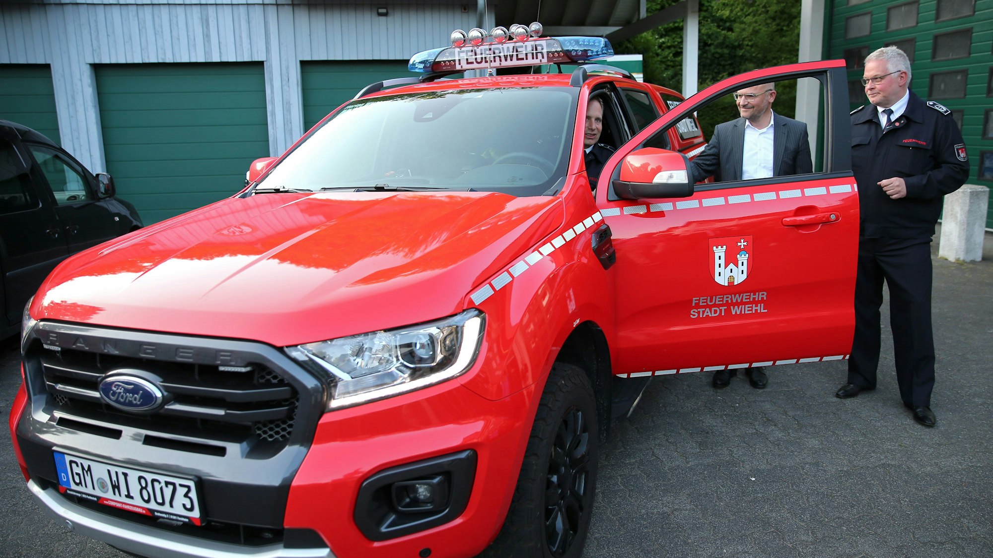 Drei Männer stehen an einem knallroten Feuerwehrauto in Form eines SUV.