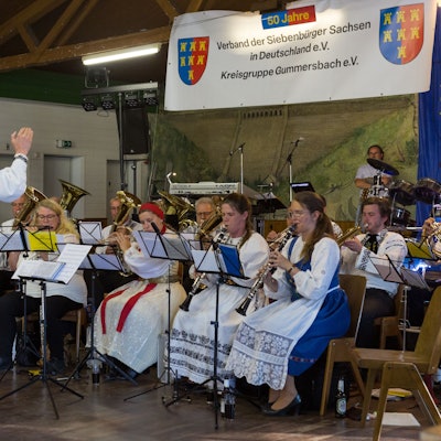 Ein Dirigent leitet ein Blasorchester, das in siebenbürgischer Tracht gekleidet ist.