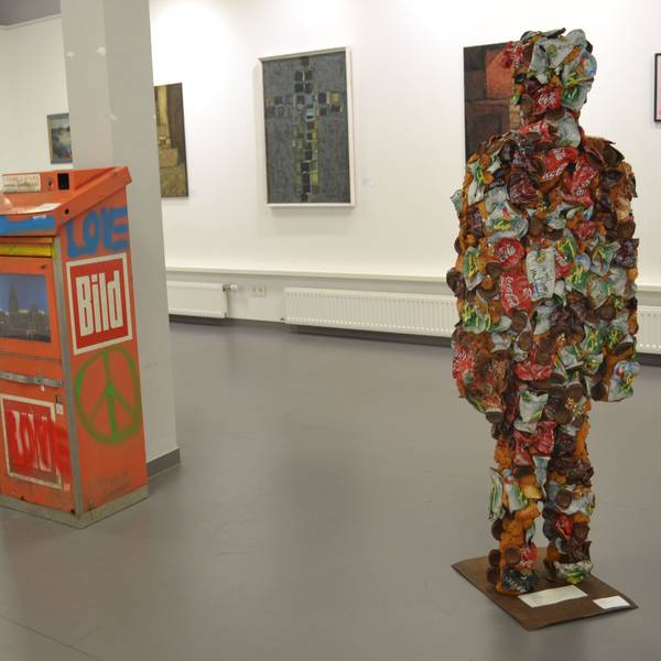 Eine Figur aus Müll steht inmitten einer Ausstellung.