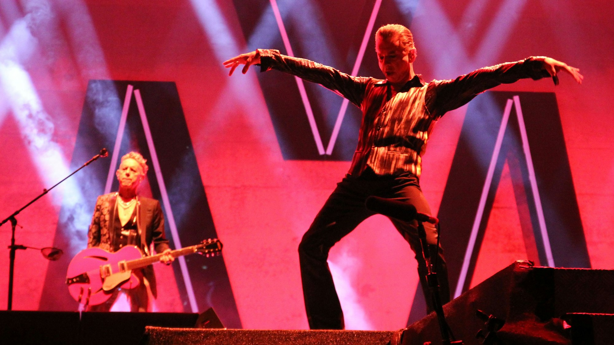 Dave Gahan (rechts) und Martin Gore in der Merkur-Spiel-Arena in Düsseldorf am 4. Juni 2023. Gahan hält seine Arme weit ausgestreckt, Gore spielt eine pinke Gitarre.