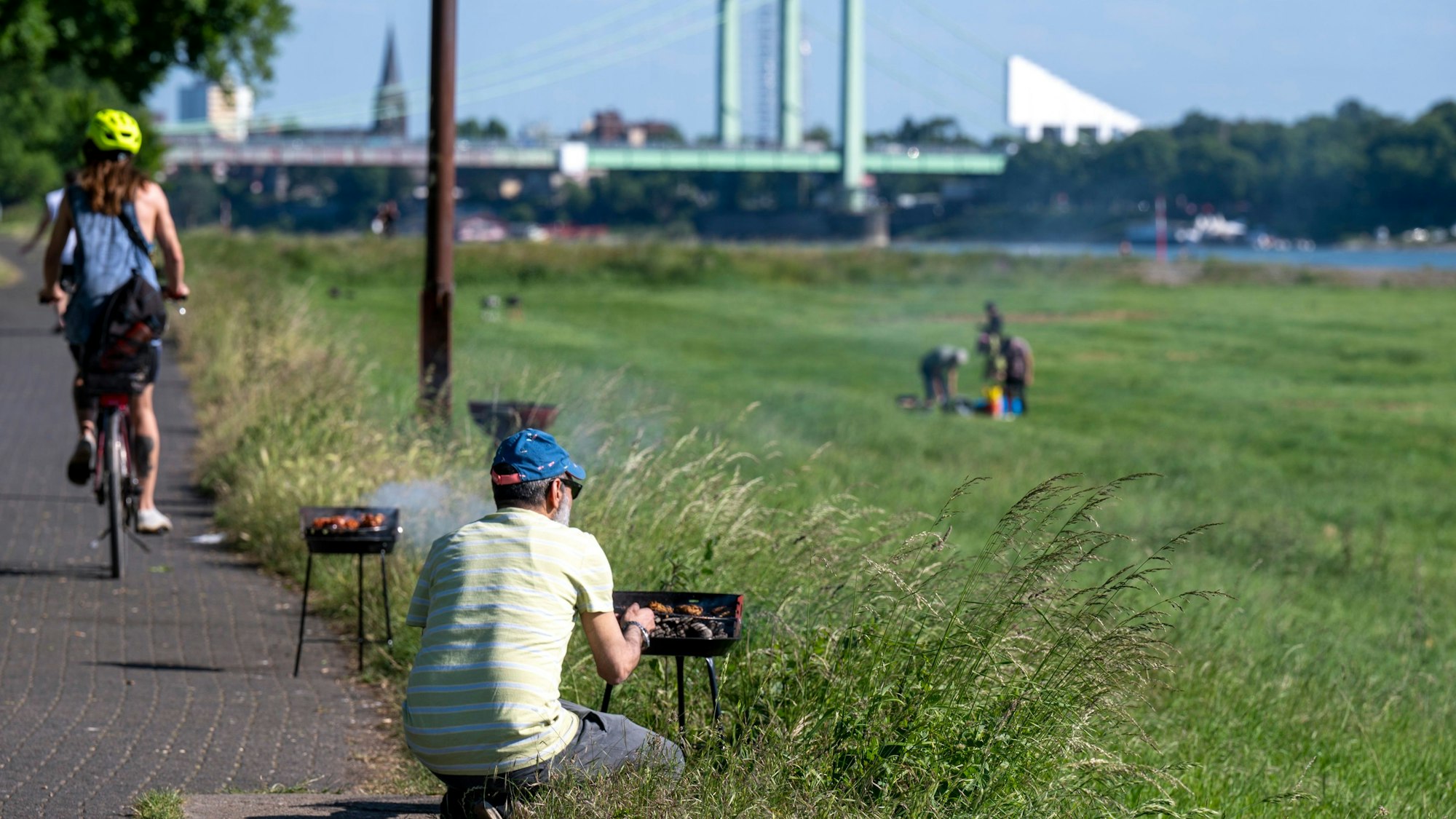 Ein Mann, zu sehen von hinten, bestückt einen Grill am Rand einer Wiese.
