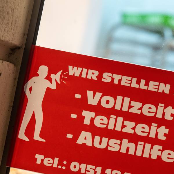 Ein rotes Schild mit der Aufschrift ·„Wir stellen ein - Vollzeit, Teilzeit, Aushilfen“ hängt an einer Eingangstür.