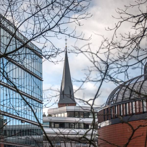 Turm der Christuskirche ragt zwischen Gebäuden in der Wiesdorfer City hervor.