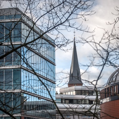 Turm der Christuskirche ragt zwischen Gebäuden in der Wiesdorfer City hervor.