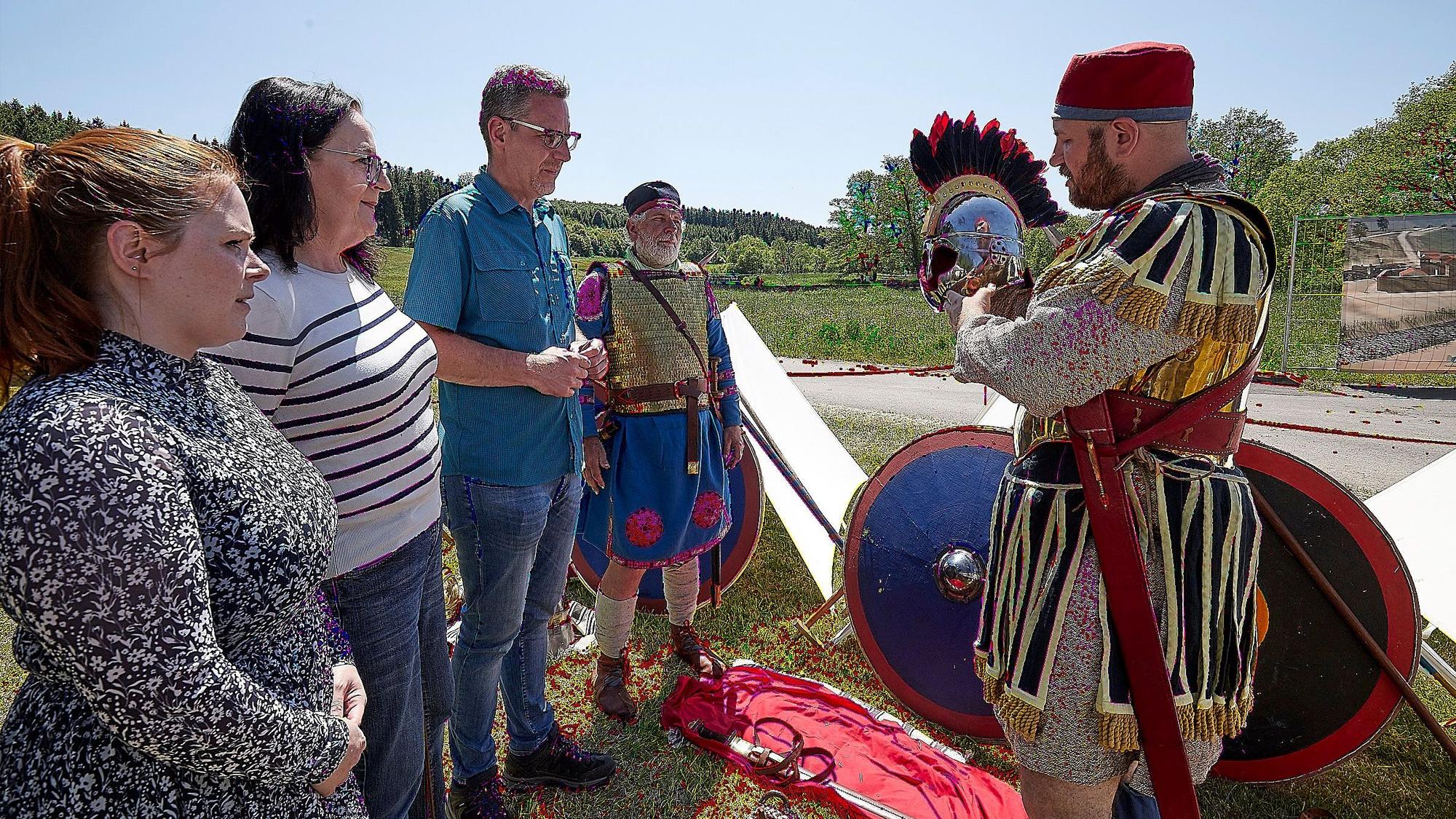 Ein Römer-Darsteller (r.) erklärt drei Besuchern seine Kleidung und den Helm.