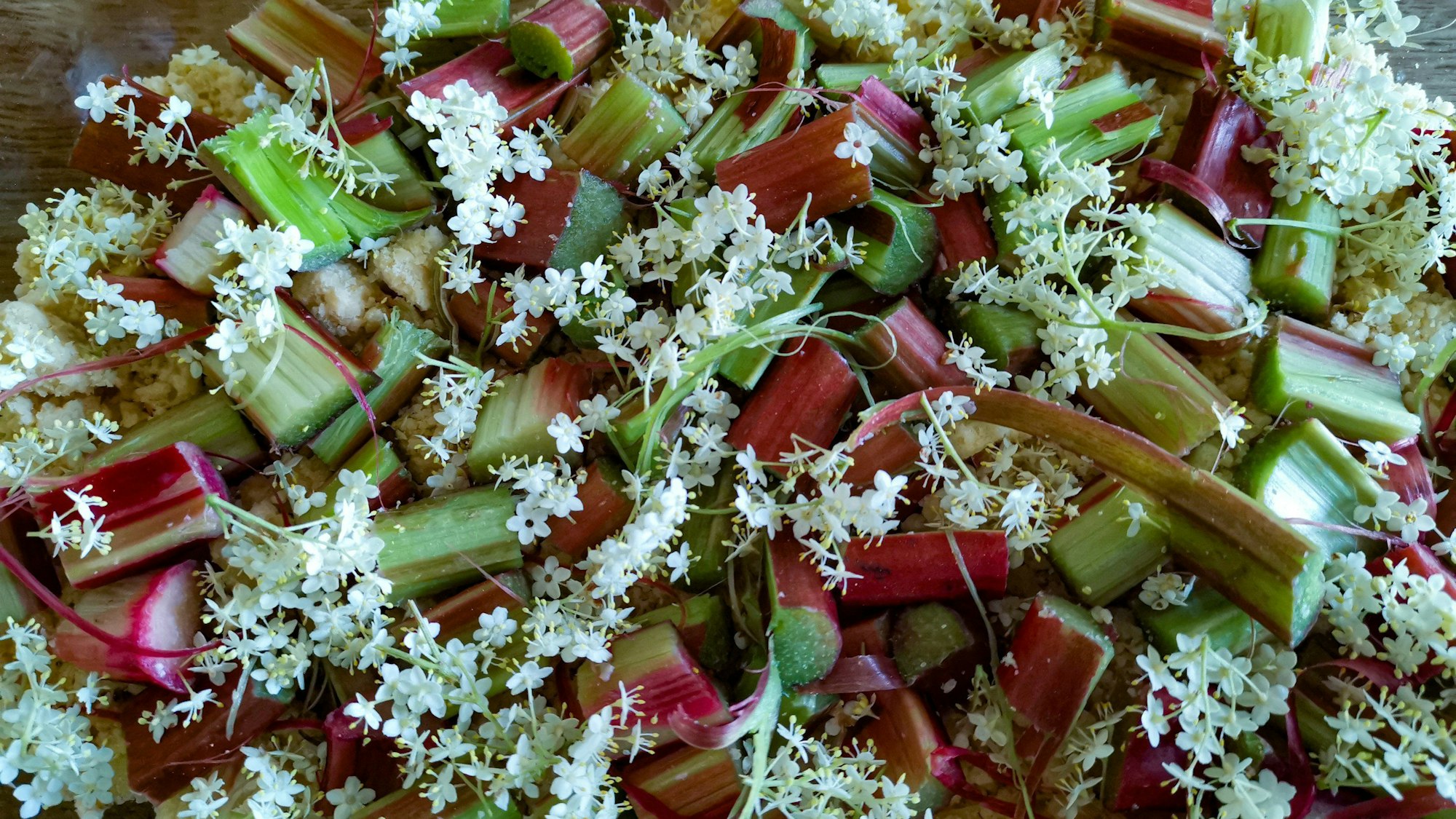 weiße Blüten liegen auf rot-grünen Rharbarber-Stücken