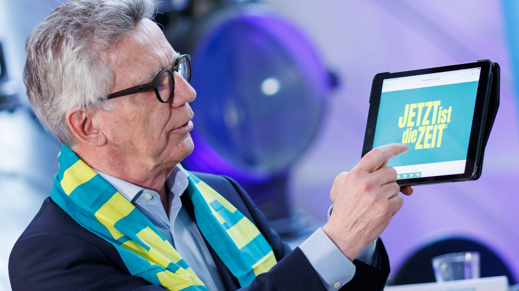Thomas de Maizière (CDU), Präsident des 38. Deutschen Evangelischen Kirchentags in Nürnberg, präsentiert auf einem Tablet die Programm-App. Um den Hals trägt er einen Kirchentagsschal mit dem Motto „Jetzt ist die Zeit“.