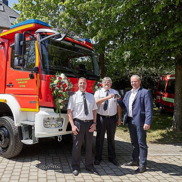 Löschgruppenführer Jochen Völler (v.l.), Kalls Feuerwehrchef Harald Heinen und Kalls Bürgermeister Hermann-Josef Esser stehen vor dem neuen Feuerwehrfahrzeug. Esser übergibt Heinen den Schlüssel.