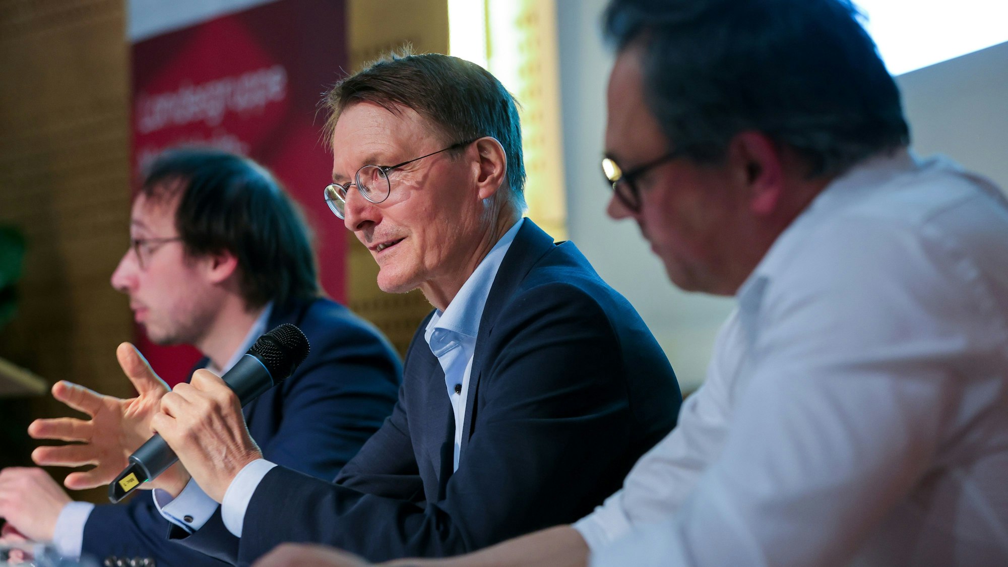 Im Bild v.l.n.r. der Moderato, Karl Lauterbach und Christian Karagiannidis – Lauterbach spricht ins Mikrofon.