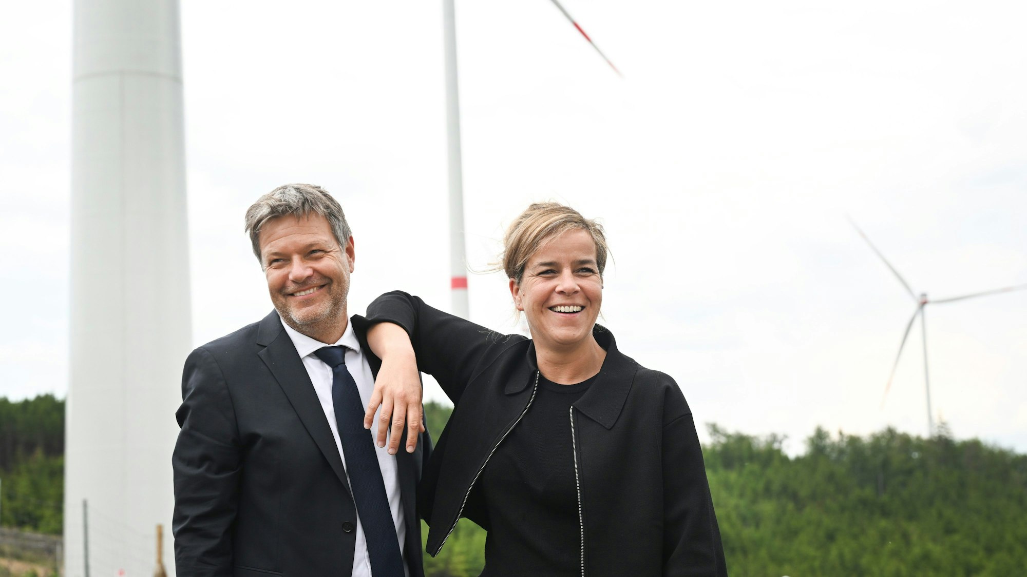 06.06.2023, Nordrhein-Westfalen, Bad Berleburg: Robert Habeck (l), Bundeswirtschaftsminister, und NRW-Wirtschaftsministerin Mona Neubaur (beide Grüne), scherzen vor Windrädern zur Stromerzeugung. Die Wittgenstein Gruppe sowie der Landesverband Erneuerbare Energien NRW nehmen den seit Herbst 2022 bestehenden Wald-Windpark Arfeld mit vier Windrädern offiziell in Betrieb. Foto: Federico Gambarini/dpa +++ dpa-Bildfunk +++