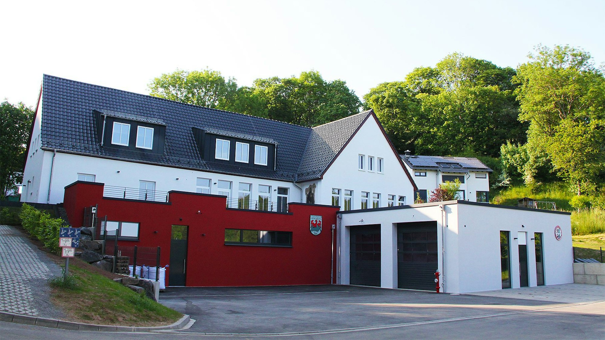 Das Bild zeigt vorne den Neubau des Feuerwehrgerätehauses in Kronenburg, dahinter und etwas erhöht im Hang das Dorfgemeinschaftshaus.